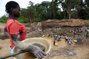 A woman stands with a containers as others sieve through the mud to find gold dust, on May 5, 2014 at the Gam gold mine, in Gaga, in the western part of the Central African Republic.